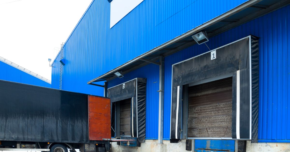 The back of a building has two loading docks. One dock has the back of a semi truck parked next to it.