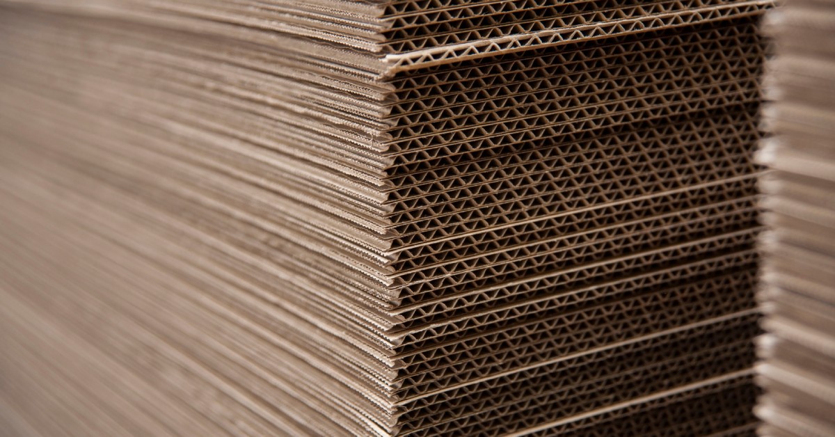 A stack of corrugated cardboard all in one pile. The cardboard is unfolded and flattened.