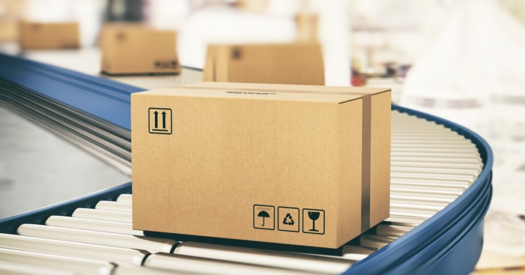 A cardboard box is on a conveyor belt. There is writing on the box and arrows saying which way is up.