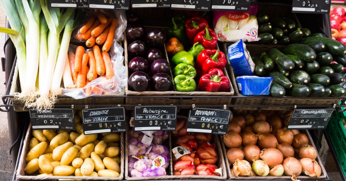 There are several shelves of produce in different bins. Among the produce are peppers, carrots, and potatoes.