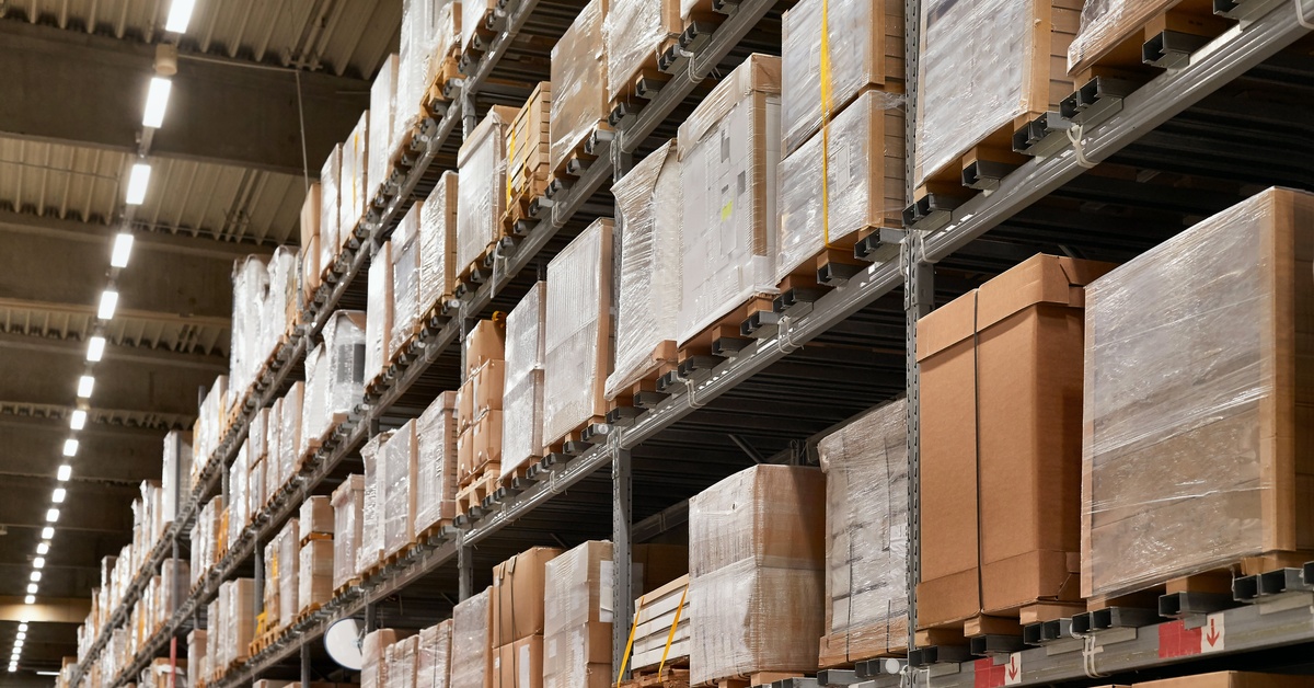 A warehouse with many tiers of storage shelving. There are many boxes stacked on the shelving units.