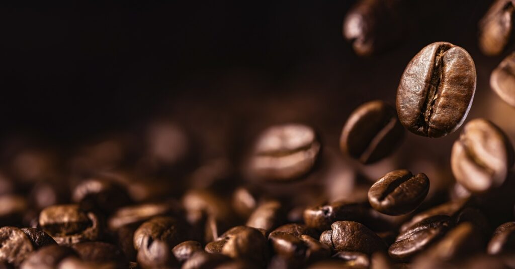 A closeup view of a pile of coffee beans. The background is dark and in shadow.