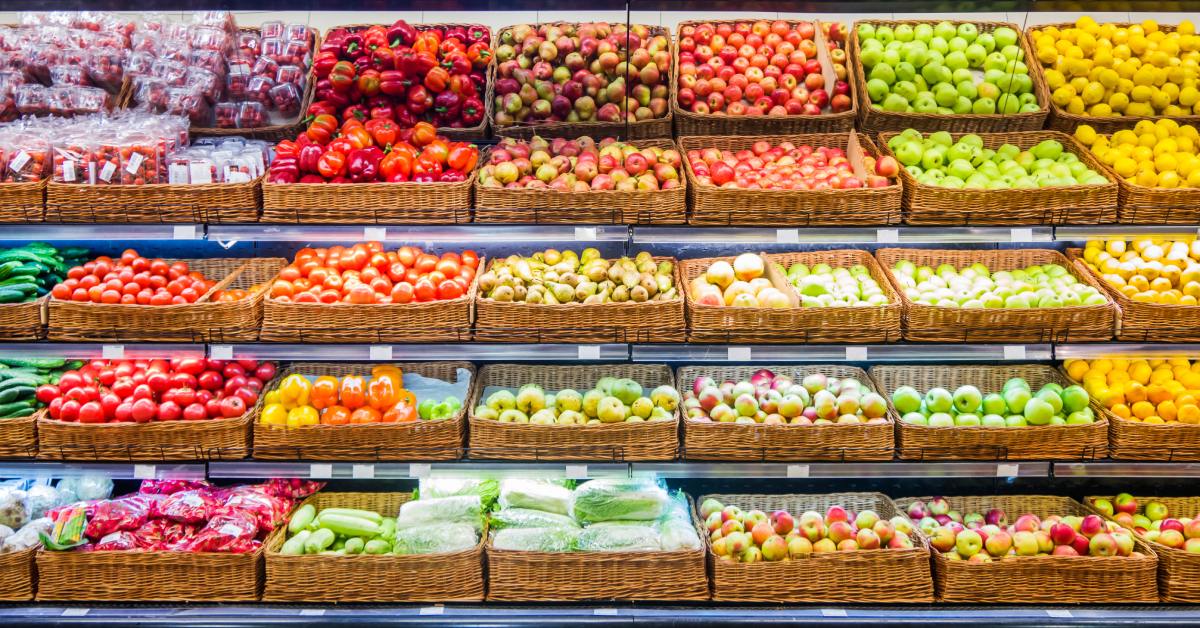 A large produce section of a market features shelves of colorful cucumbers, apples, peppers, and pears.