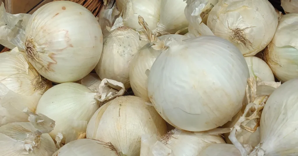 There are several white onions in a basket. The onions are peeling and the basket is made of wood.