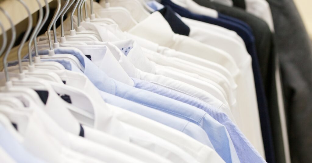 A row of clothes on hangars are hanging from a metal pole. Some of the clothes have blue fabric.