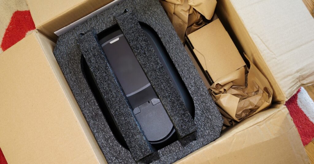 A black item is in a cardboard box. The item in the box has a protective insert and a smaller box next to it.