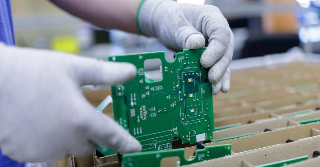 A person who is wearing gloves is placing a printed circuit board into a cardboard box that has other boards in it.