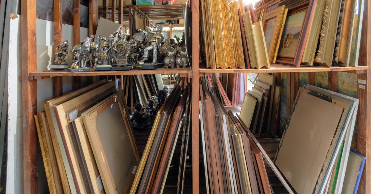 There are several picture frames that are placed against each other. There is another shelf with little statues.