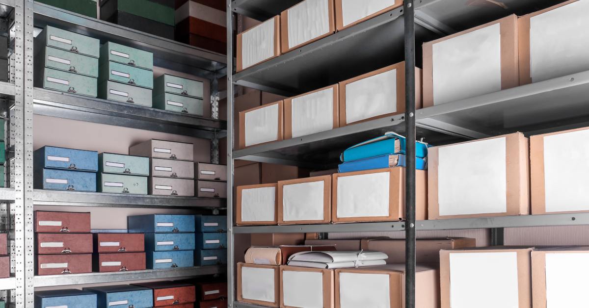 A room with several shelves that have cardboard boxes. Some of the boxes have pieces of paper on them.