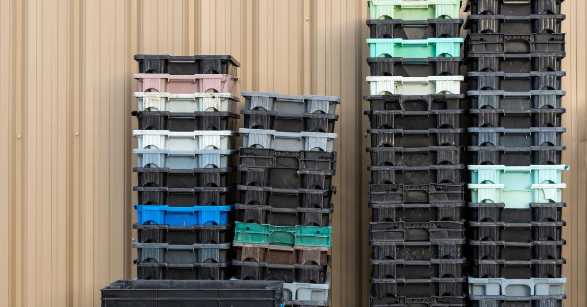 There are several stacks of food totes, and each stack is pushed up against a wall. The stacks are all different heights.