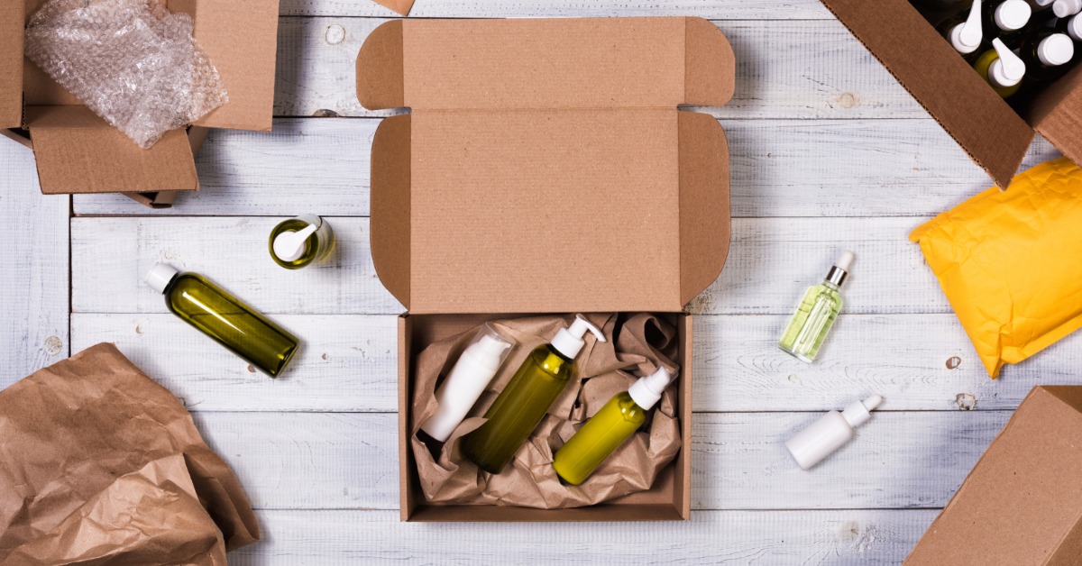Cosmetic supplies are inside a cardboard box. The box is on a table and surrounded by other boxes.