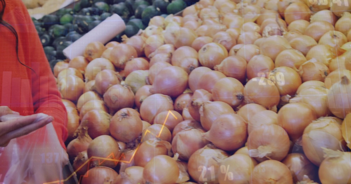 A produce bin is filled with onions. There is a person next to the bin who is putting onions in a bag.