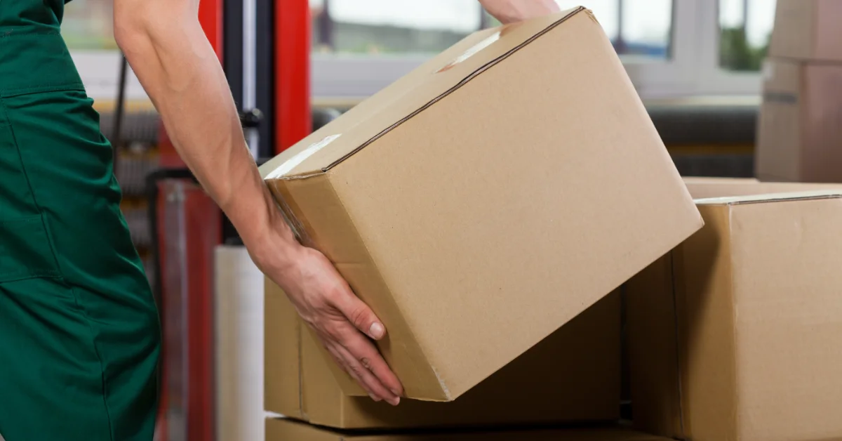 A person is lifting a cardboard box. There is a stack of boxes underneath the one the person is lifting.