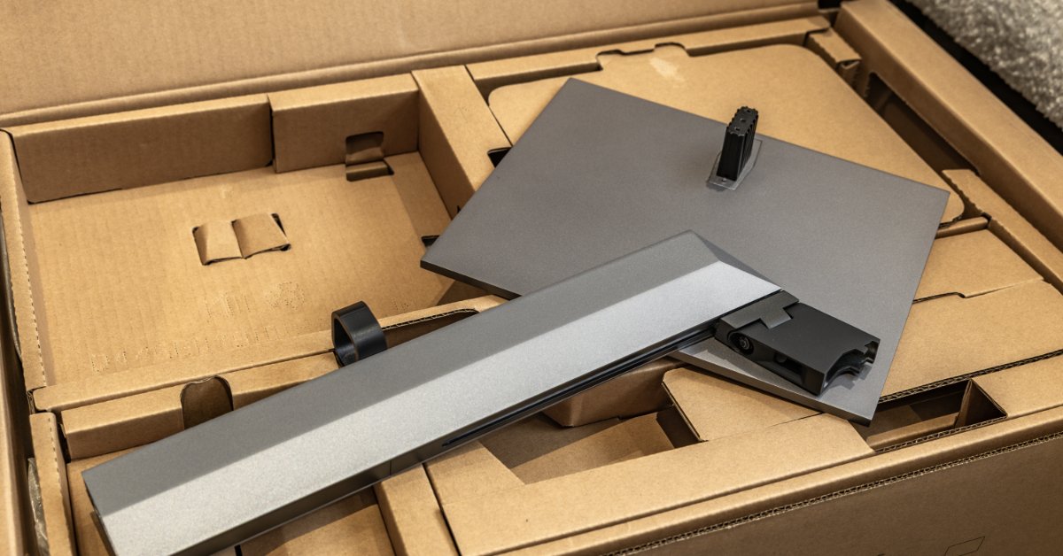 An electronic is partially pulled out of a cardboard box. The electronic is in two pieces; one square piece and a longer rectangular one.