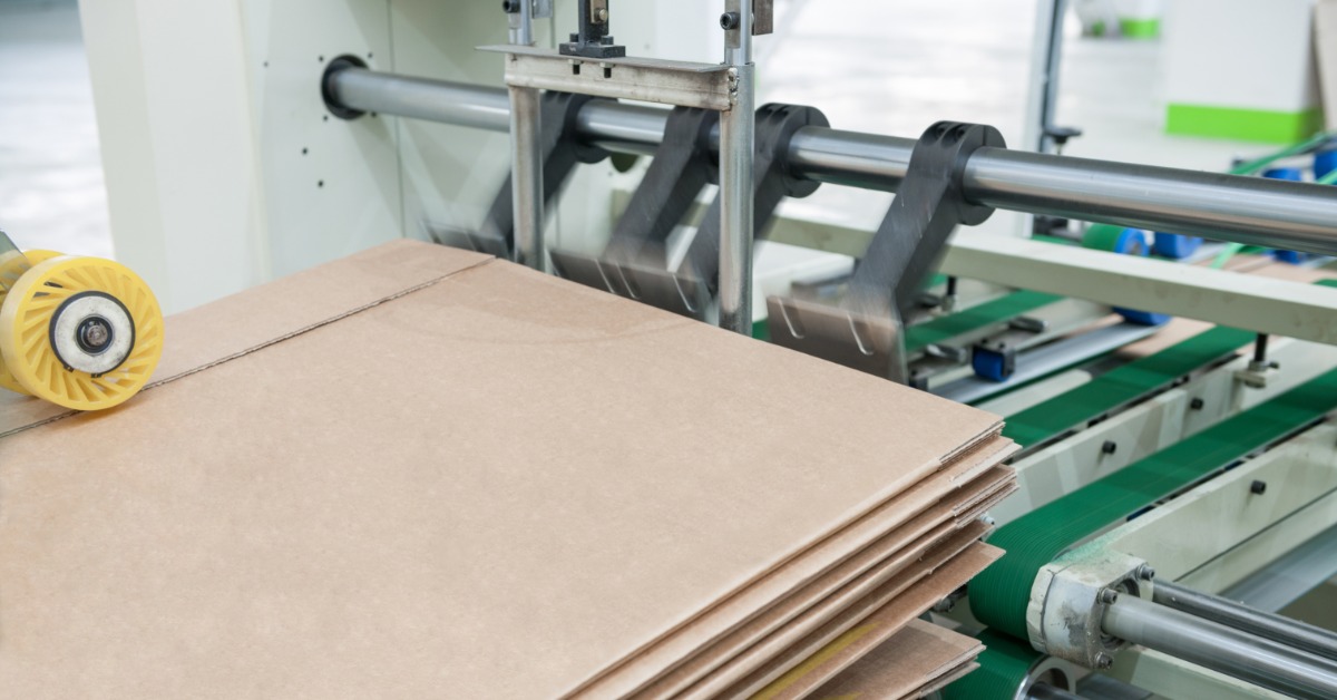 Several sheets of cardboard are stacked on top of each other. There is some industrial equipment to the right of the cardboard.
