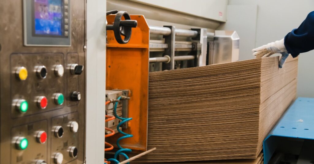 A stack of unfolded cardboard is sitting on a machine. There is a person with a gloved hand that is touching the cardboard stack.