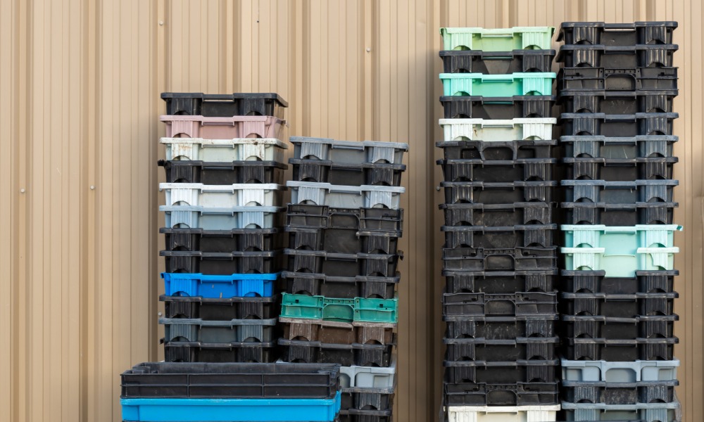 Food trays are stacked into several different stacks. Most of the trays are black but there are others that are blue.