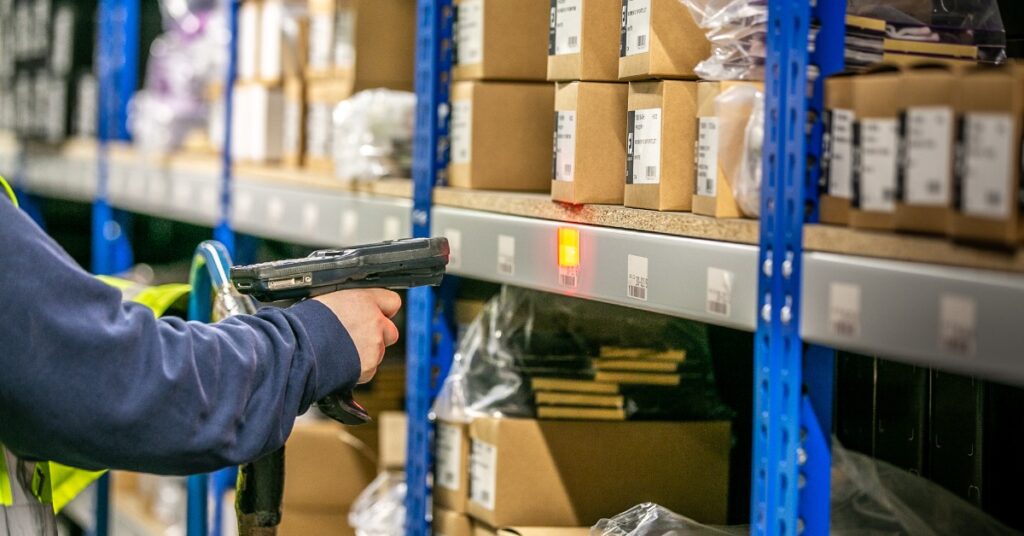 A person is using a scan gun to scan barcodes that are attached to pallet racks. There are boxes on the racks.
