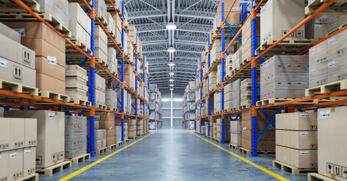 A warehouse with pallet racks on either side of a walkway. The racks are filled with pallets and boxes.