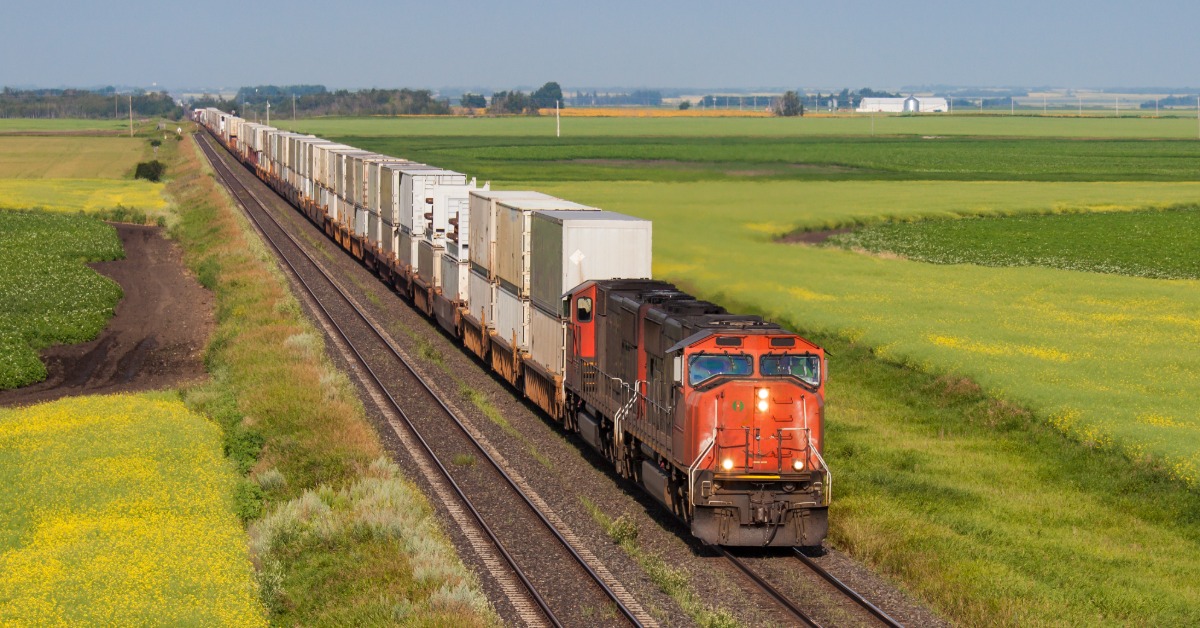 A train is going down the tracks in a grassy area. The train is pulling dozens of cars of freight behind it.