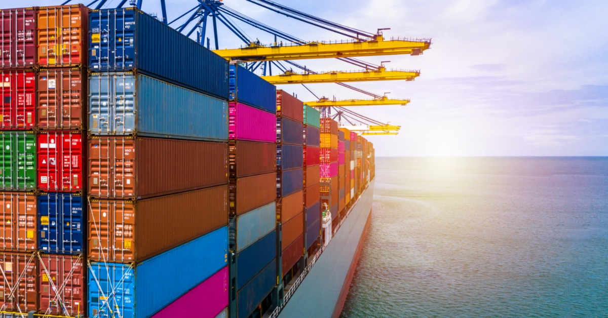 A view of the side of a container ship. It is filled to capacity with shipping containers of various colors.