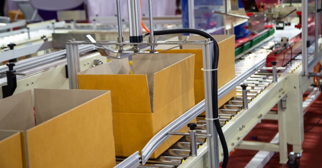 Several open cardboard boxes are on a conveyor belt. The boxes are in an industrial setting.