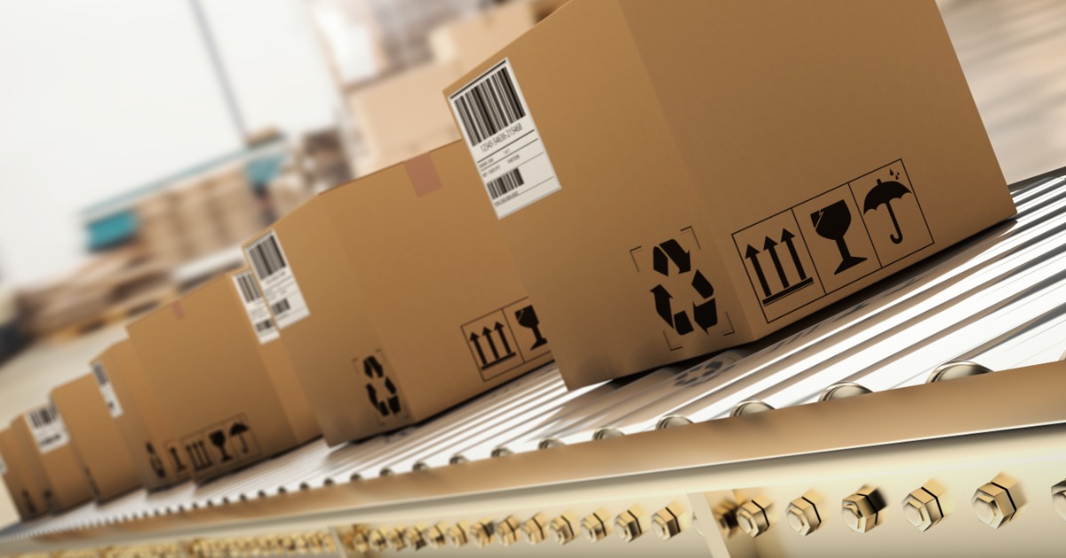 Several cardboard boxes are on an assembly line. All the boxes have marking on them.